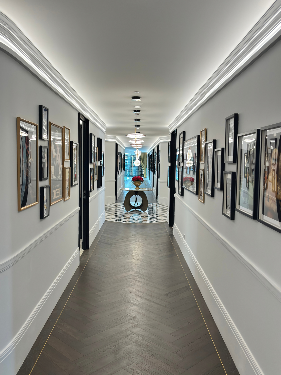 Long corridor with cove lighting, herringbone timber floor and framed artworks